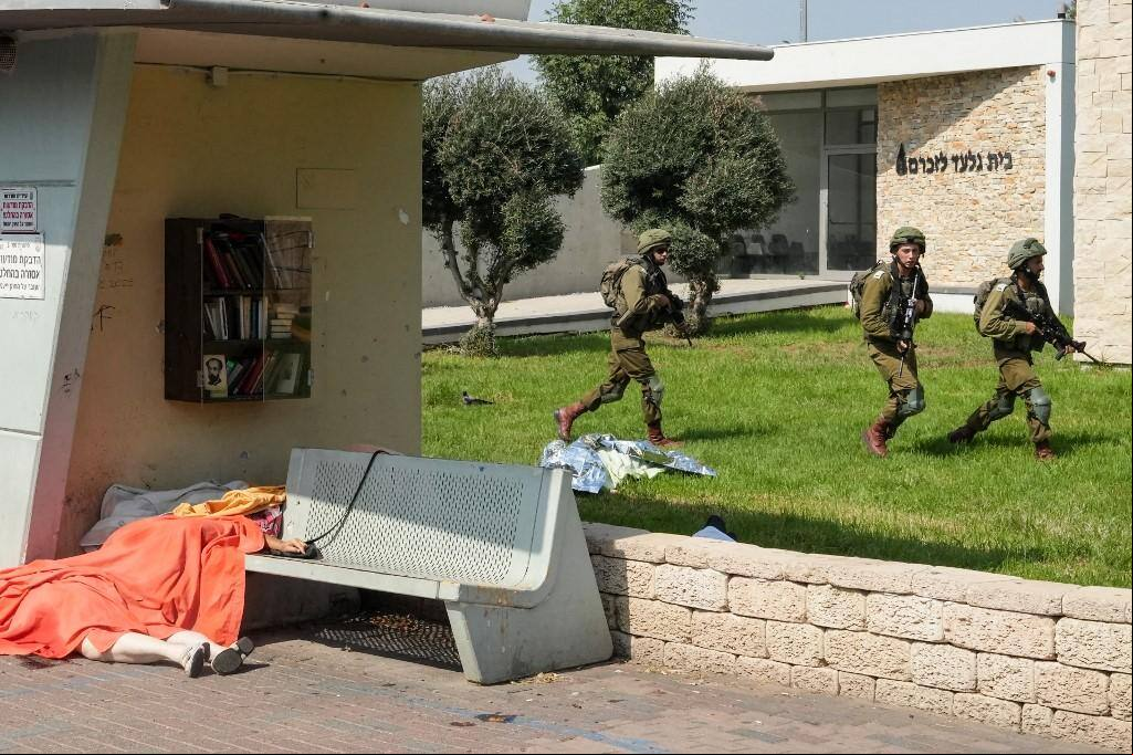 Soldados israelenses protegem uma área enquanto corpos de civis mortos em um ataque militante palestino estão cobertos na cidade de Sderot, no sul de Israel, em 7 de outubro de 2023